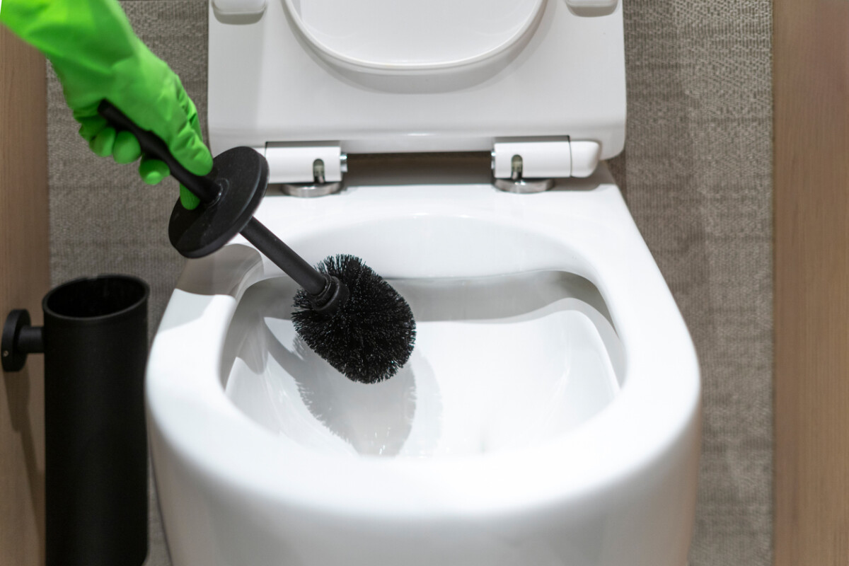 Close up of woman hand in glove with brush washing toilet bowl in restroom